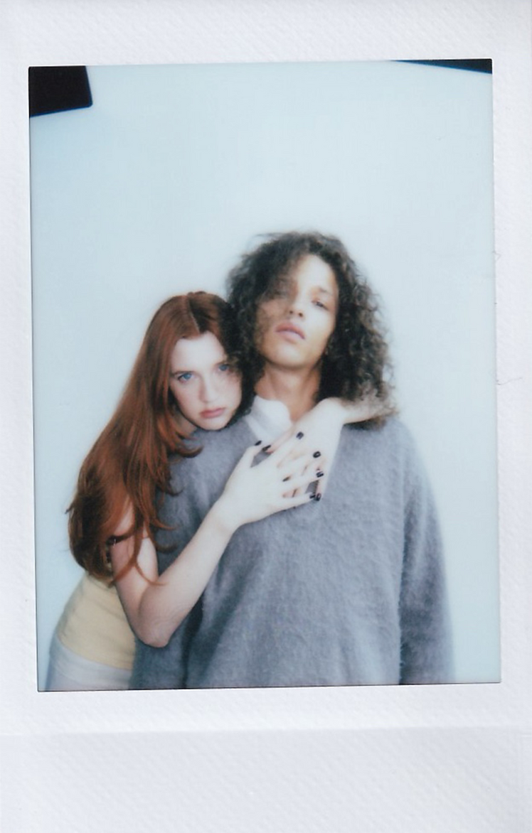 Polaroid of two people embracing, one with long red hair and one with dark curls.