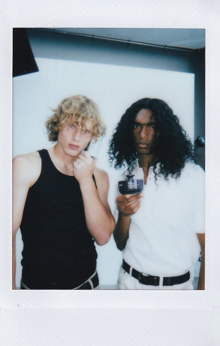 Polaroid of two men in a studio, one with blonde curls and one with long dark curls.