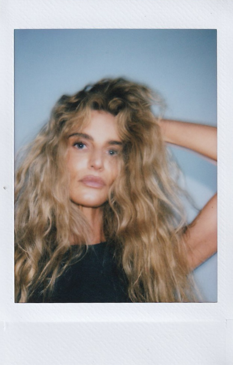 Polaroid of a woman with long, tousled blonde hair, hand in her hair.