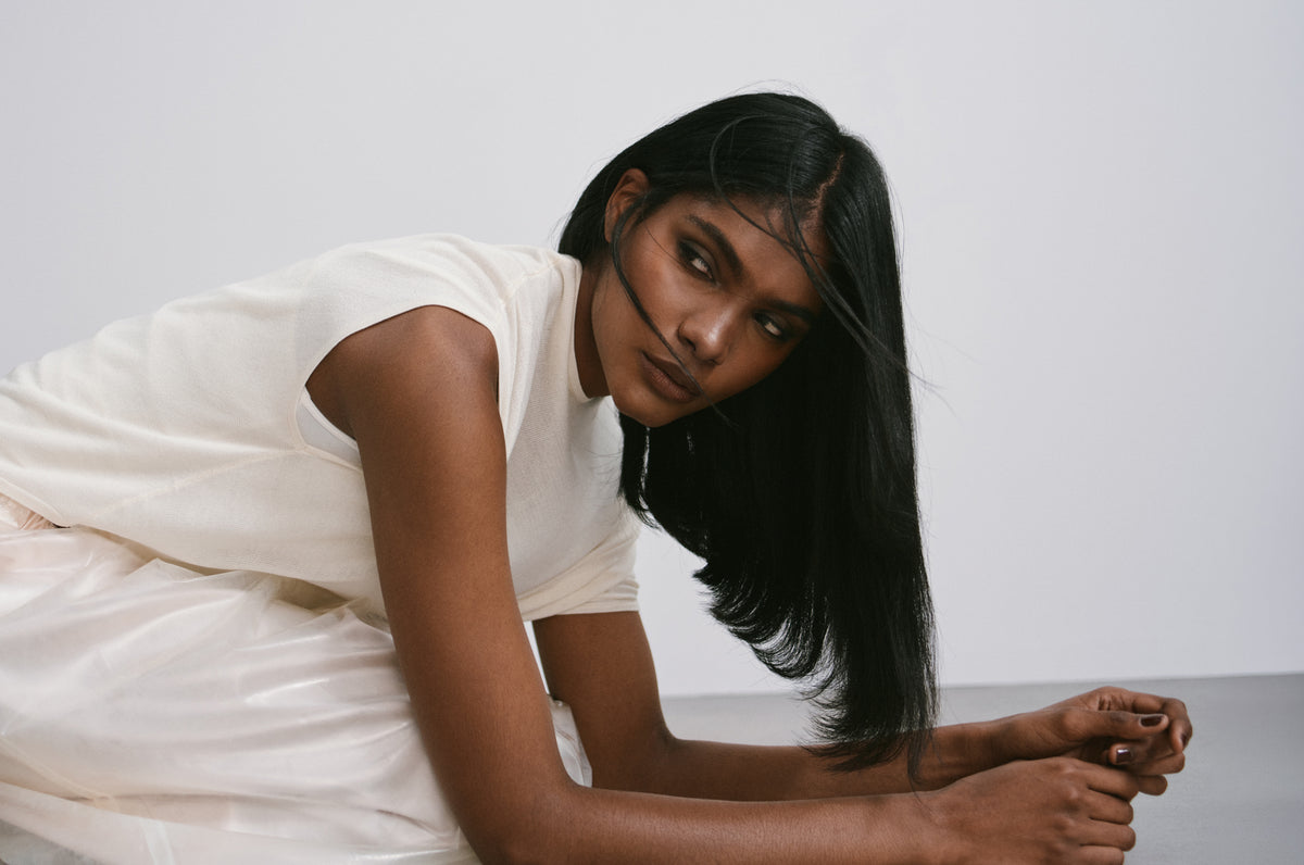 A woman with long dark hair in a white dress, leaning on the floor.