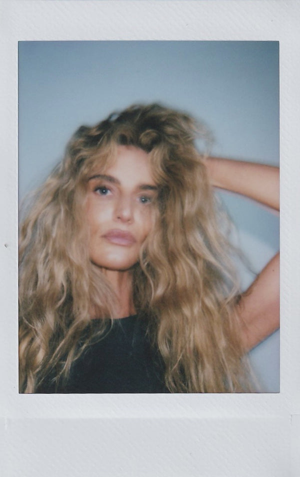 Polaroid of a woman with long, tousled blonde hair, hands in her hair.