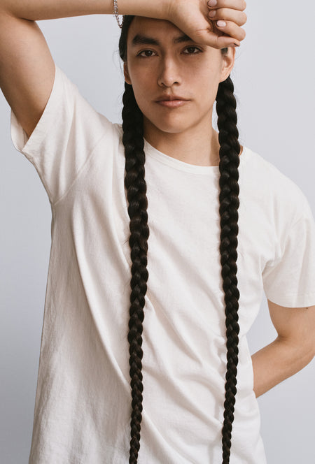 A man with two long braids, hand resting on his forehead.