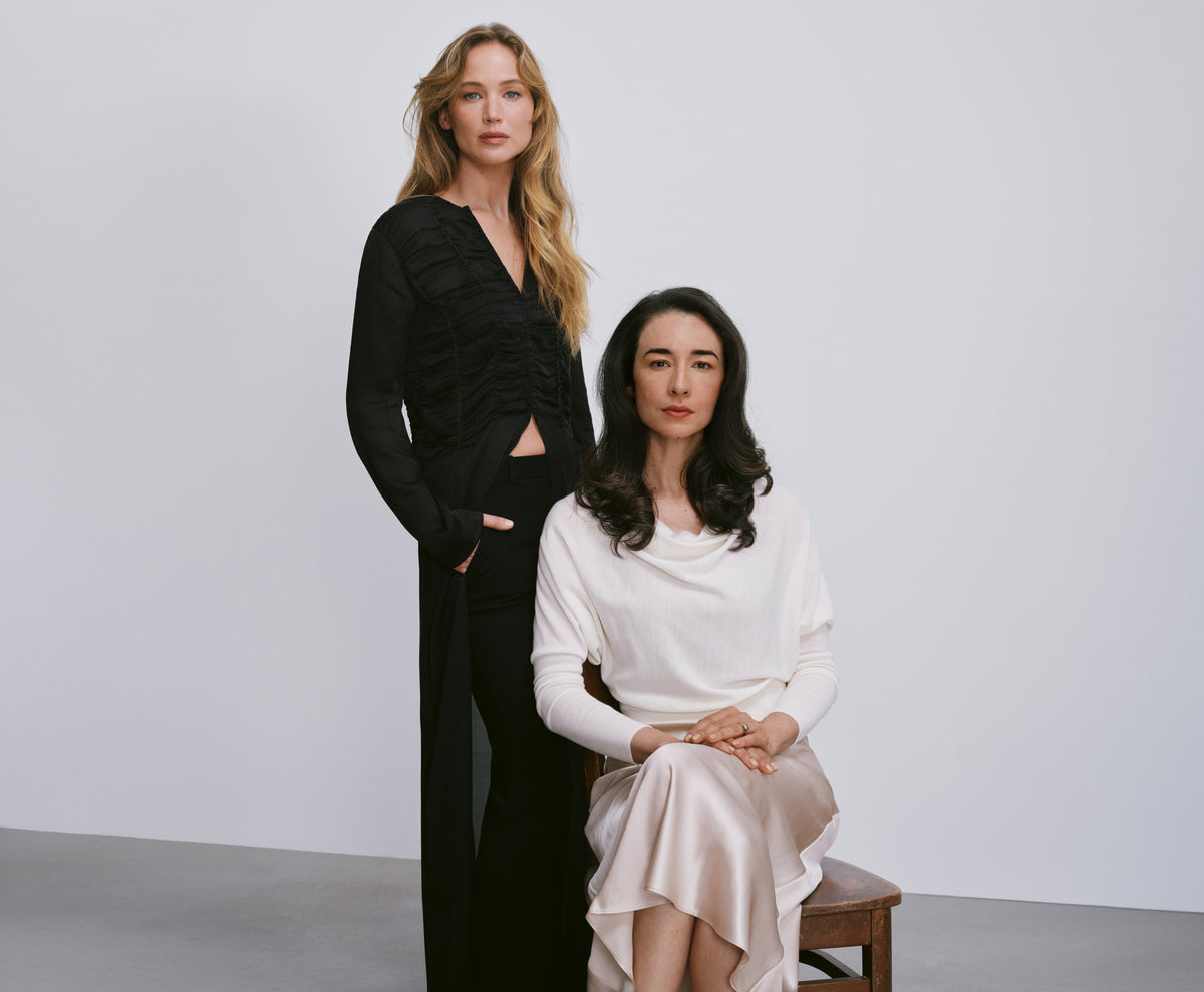 Jennifer Lawrence standing beside Jasmina Aganovic, founder of Arcaea, who is seated.